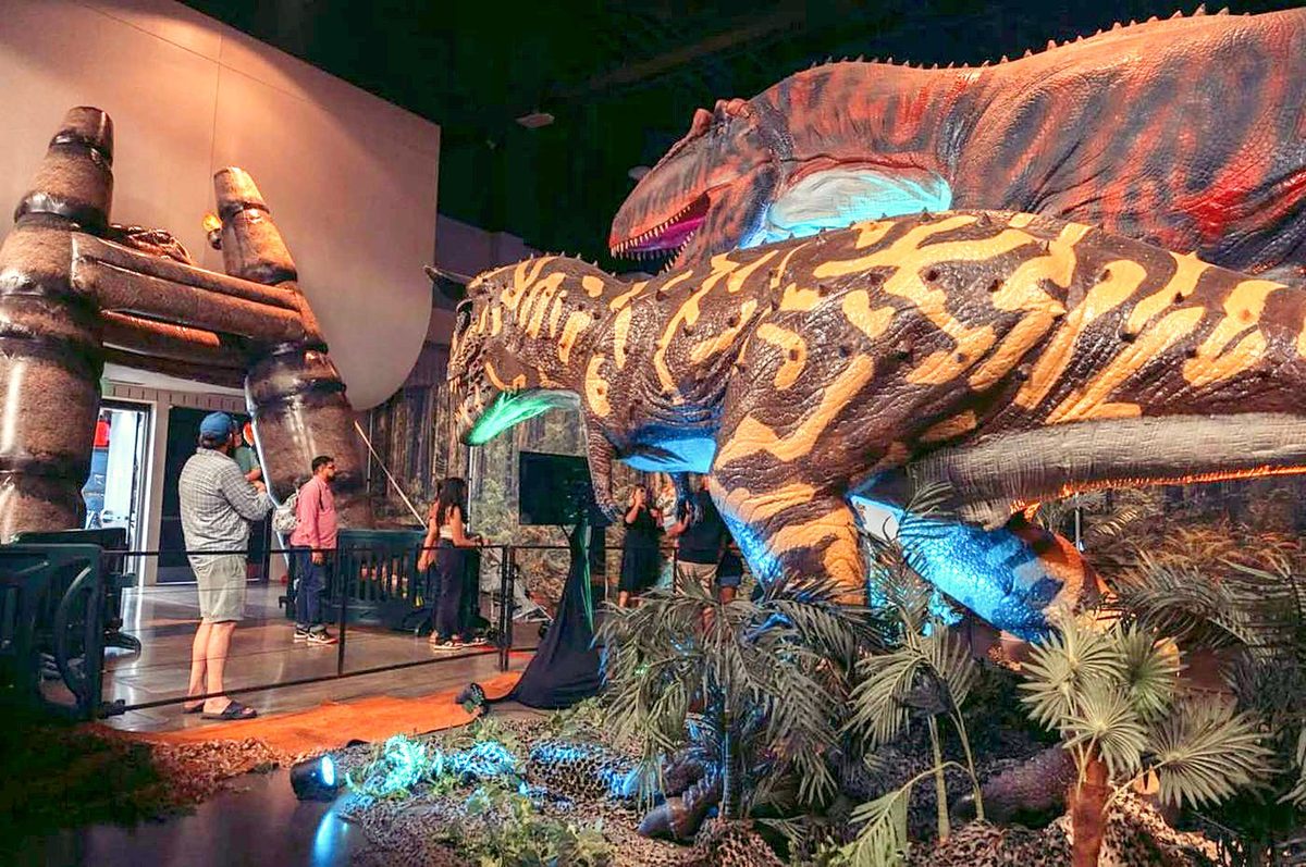 A life-size T. rex and Spinosaurus in a prehistoric jungle